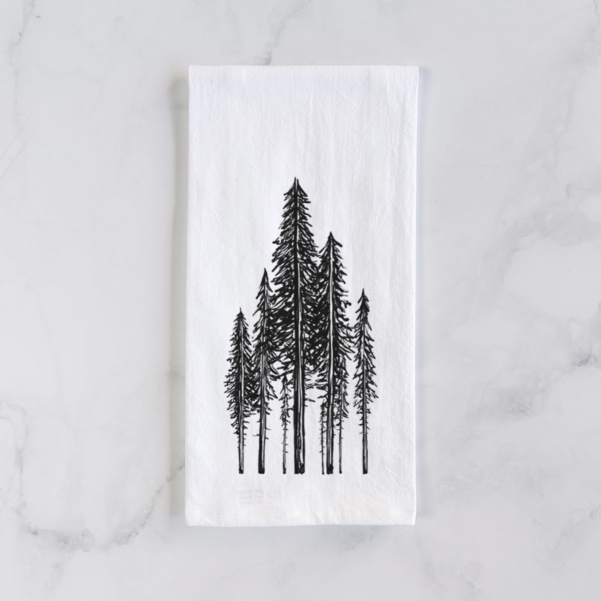 White cotton tea towel laid flat on marble, printed with a black ink illustration of a stand of tall coastal redwood trees with slender trunks and layered branches.