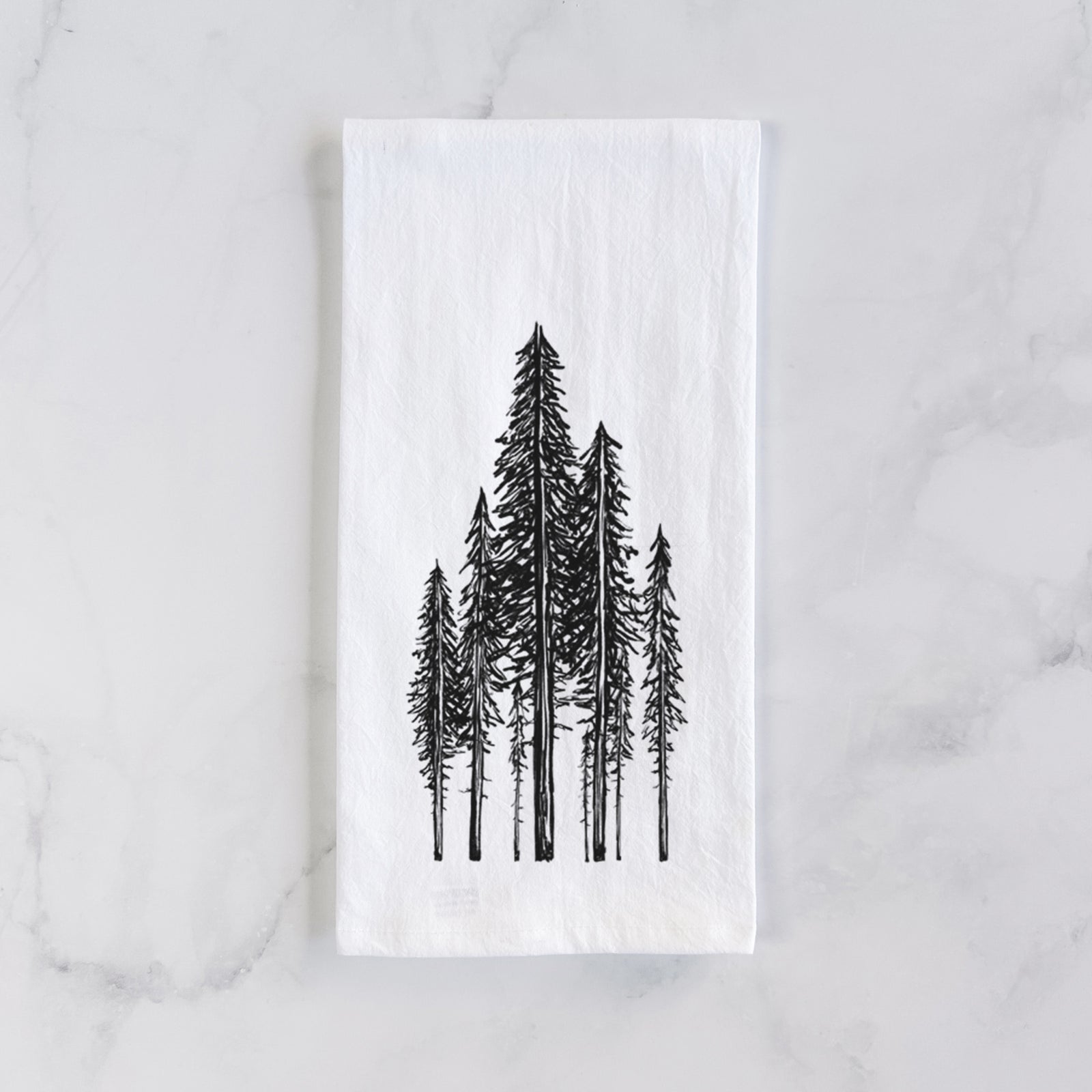 White cotton tea towel printed with a black ink illustration of a stand of tall coastal redwood trees with slender trunks and layered branches, on a marble counter beside a round wooden cutting board and greenery.