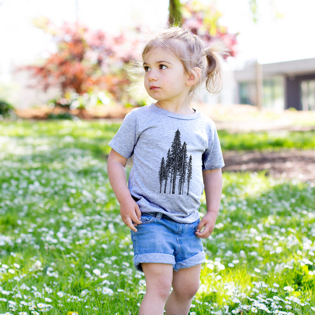 Toddler girl walking outdoors wearing a t-shirt printed with a black ink illustration of a stand of tall coastal redwood trees with slender trunks and layered branches.