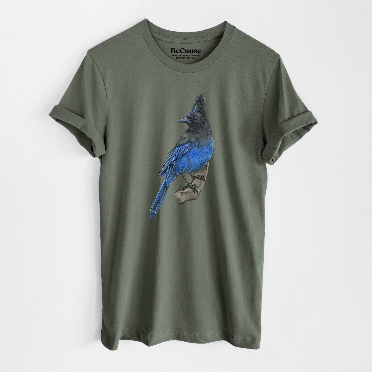 Military green lightweight cotton t-shirt laid flat, printed with a full-color illustration of a Steller's jay perched with its dark crest raised.