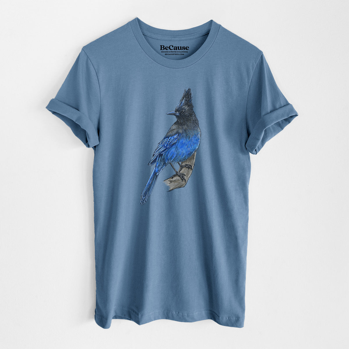Steel blue lightweight cotton t-shirt laid flat, printed with a full-color illustration of a Steller's jay perched with its dark crest raised.