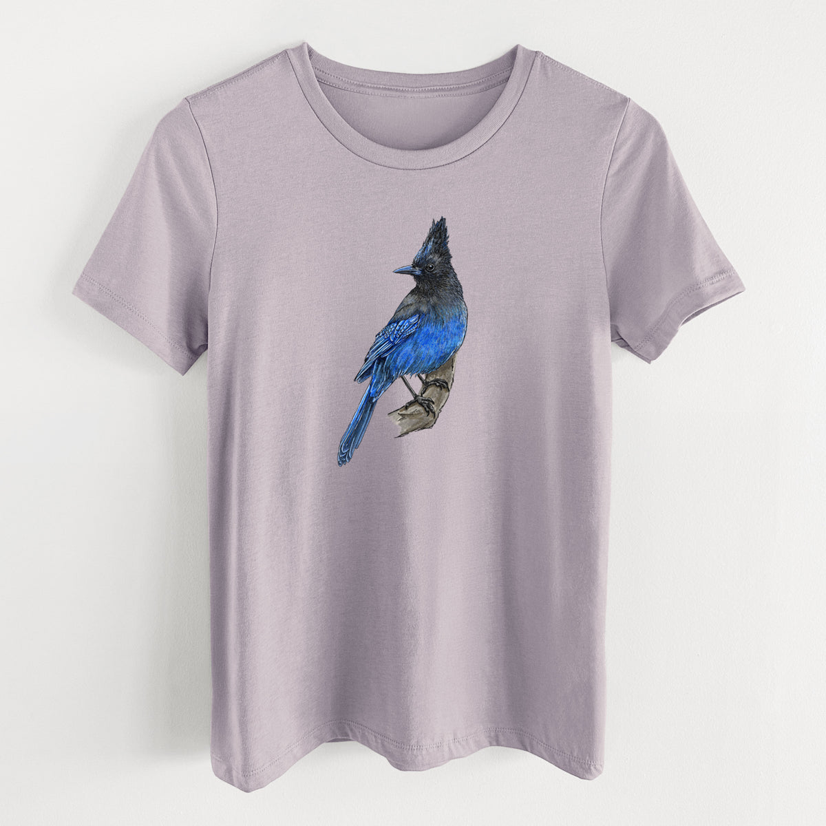 Light violet women's relaxed fit cotton t-shirt laid flat, printed with a full-color illustration of a Steller's jay perched with its dark crest raised.