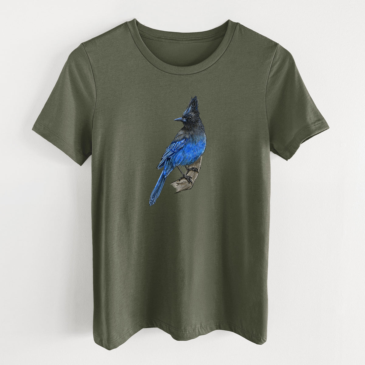 Military green women's relaxed fit cotton t-shirt laid flat, printed with a full-color illustration of a Steller's jay perched with its dark crest raised.