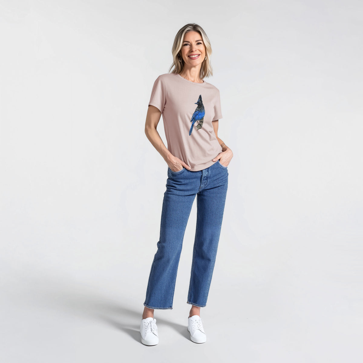 Woman wearing a pink gravel women's relaxed fit cotton t-shirt printed with a full-color illustration of a Steller's jay perched with its dark crest raised.