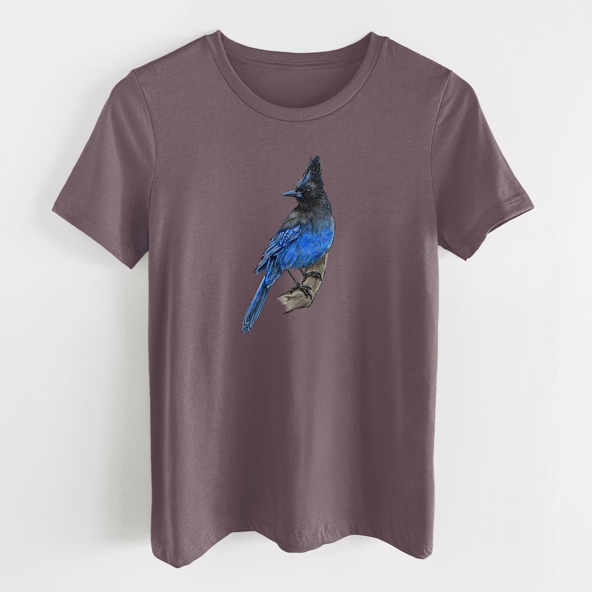 Purple storm women's relaxed fit cotton t-shirt laid flat, printed with a full-color illustration of a Steller's jay perched with its dark crest raised.