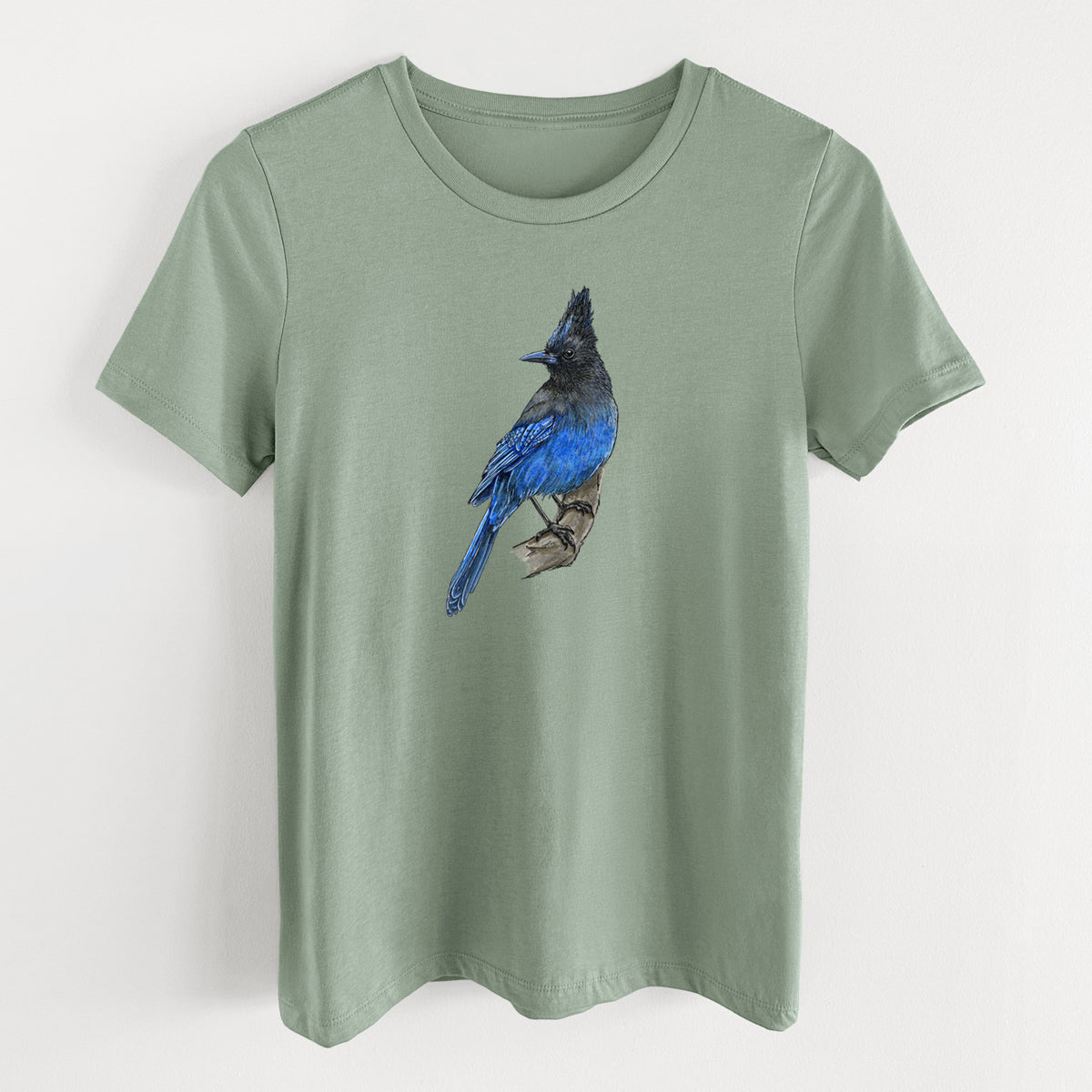 Sage green women's relaxed fit cotton t-shirt laid flat, printed with a full-color illustration of a Steller's jay perched with its dark crest raised.