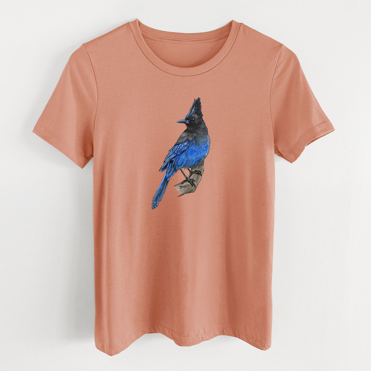 Terracotta orange women's relaxed fit cotton t-shirt laid flat, printed with a full-color illustration of a Steller's jay perched with its dark crest raised.