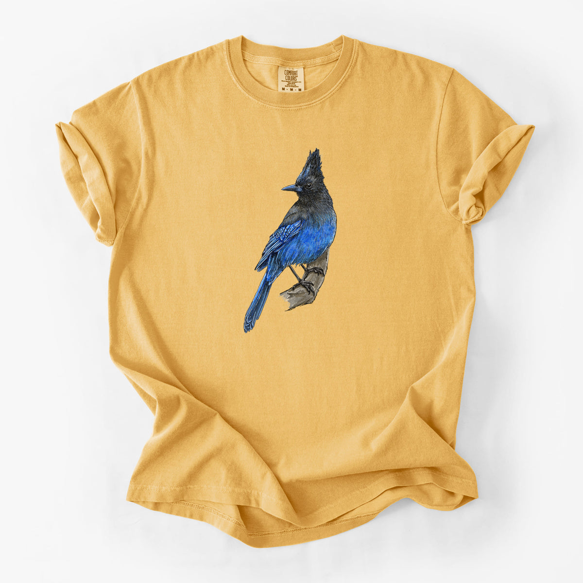 Golden wheat yellow Comfort Colors t-shirt laid flat, printed with a full-color illustration of a Steller's jay perched with its dark crest raised.
