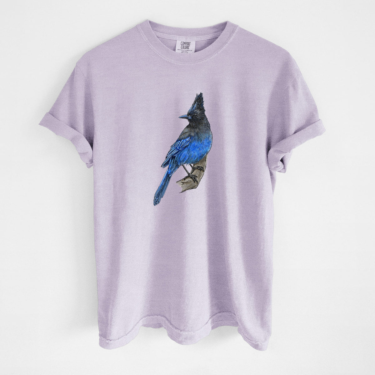 Orchid purple Comfort Colors t-shirt laid flat, printed with a full-color illustration of a Steller's jay perched with its dark crest raised.