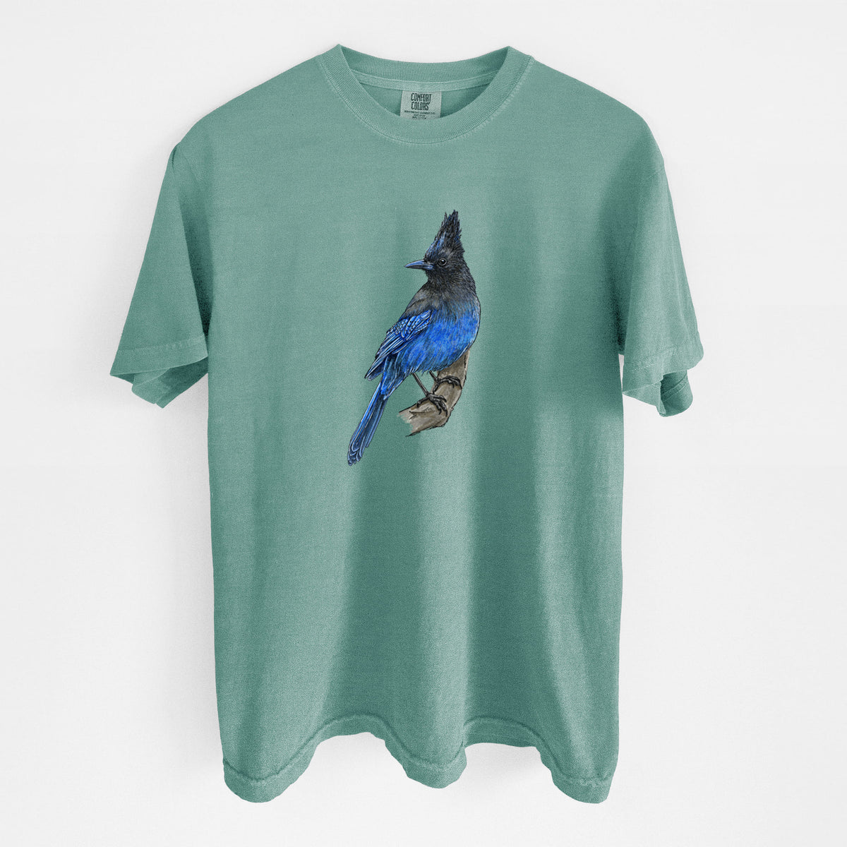 Reef green Comfort Colors t-shirt laid flat, printed with a full-color illustration of a Steller's jay perched with its dark crest raised.