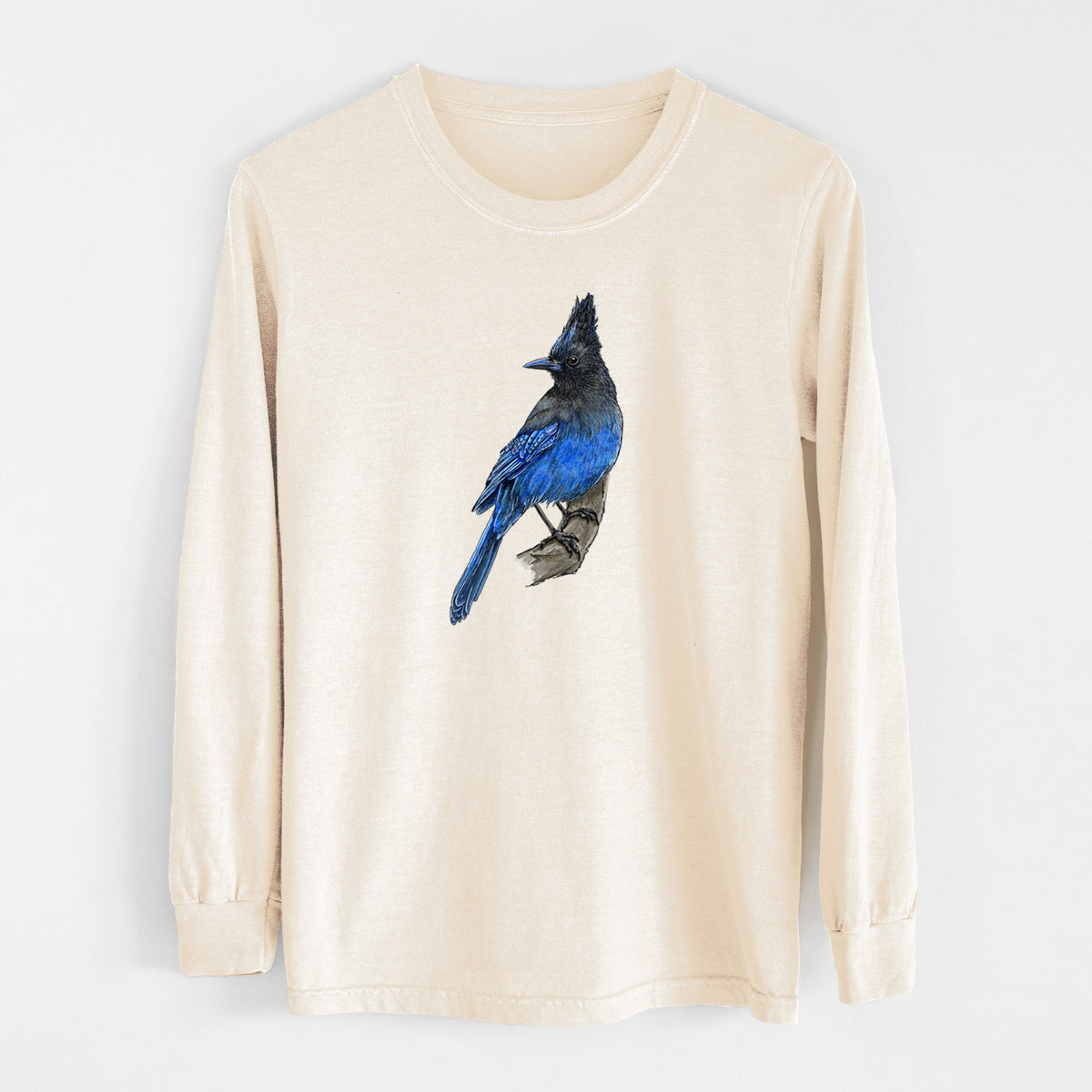 Ivory Comfort Colors long sleeve shirt laid flat, printed with a full-color illustration of a Steller's jay perched with its dark crest raised.