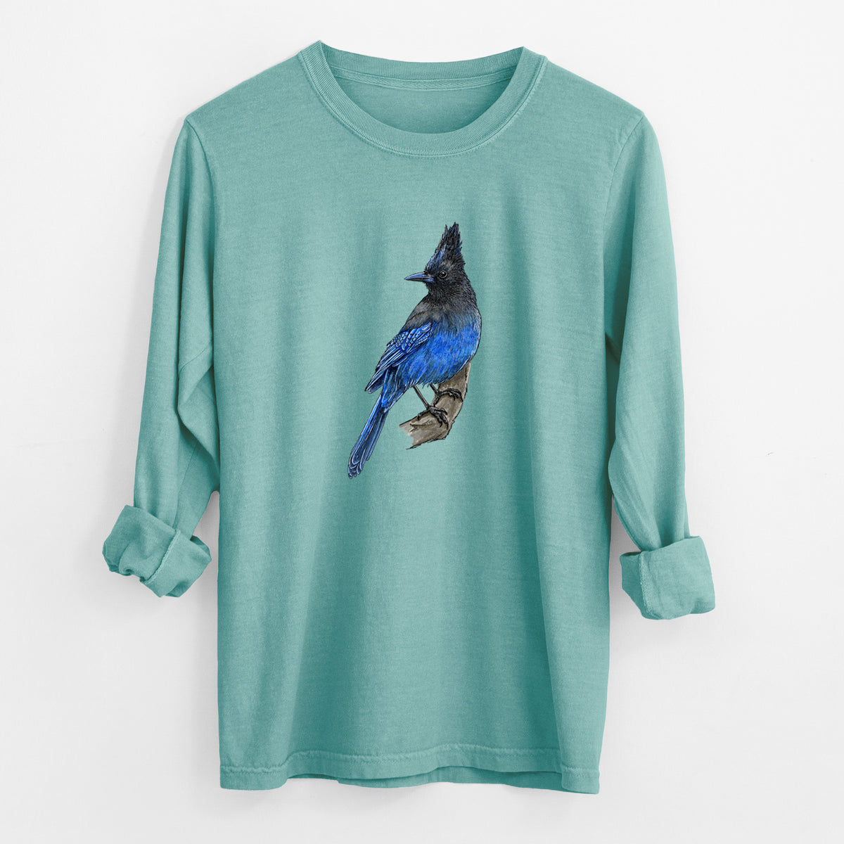 Reef green Comfort Colors long sleeve shirt laid flat with the cuffs rolled, printed with a full-color illustration of a Steller's jay perched with its dark crest raised.