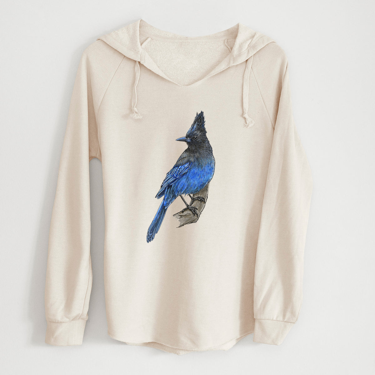 Bone cream women's Cali Wave hooded sweatshirt laid flat, printed with a full-color illustration of a Steller's jay perched with its dark crest raised.