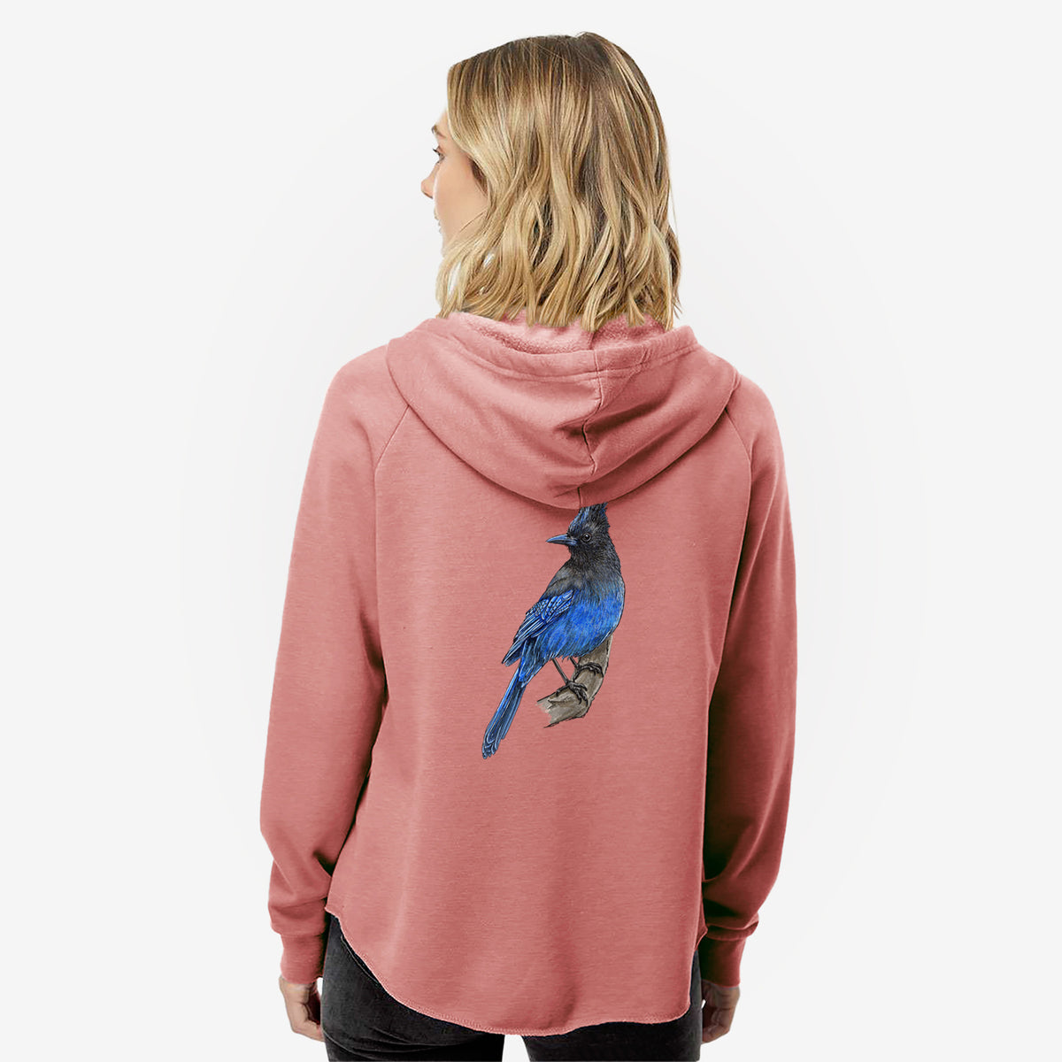 Woman wearing a dusty rose women's Cali Wave zip-up sweatshirt printed with a full-color illustration of a Steller's jay perched with its dark crest raised, seen from behind.