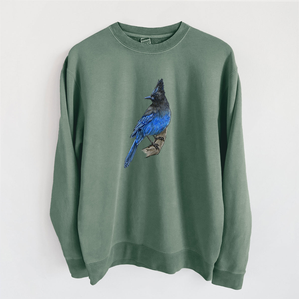 Alpine green pigment dyed crewneck sweatshirt laid flat, printed with a full-color illustration of a Steller's jay perched with its dark crest raised.