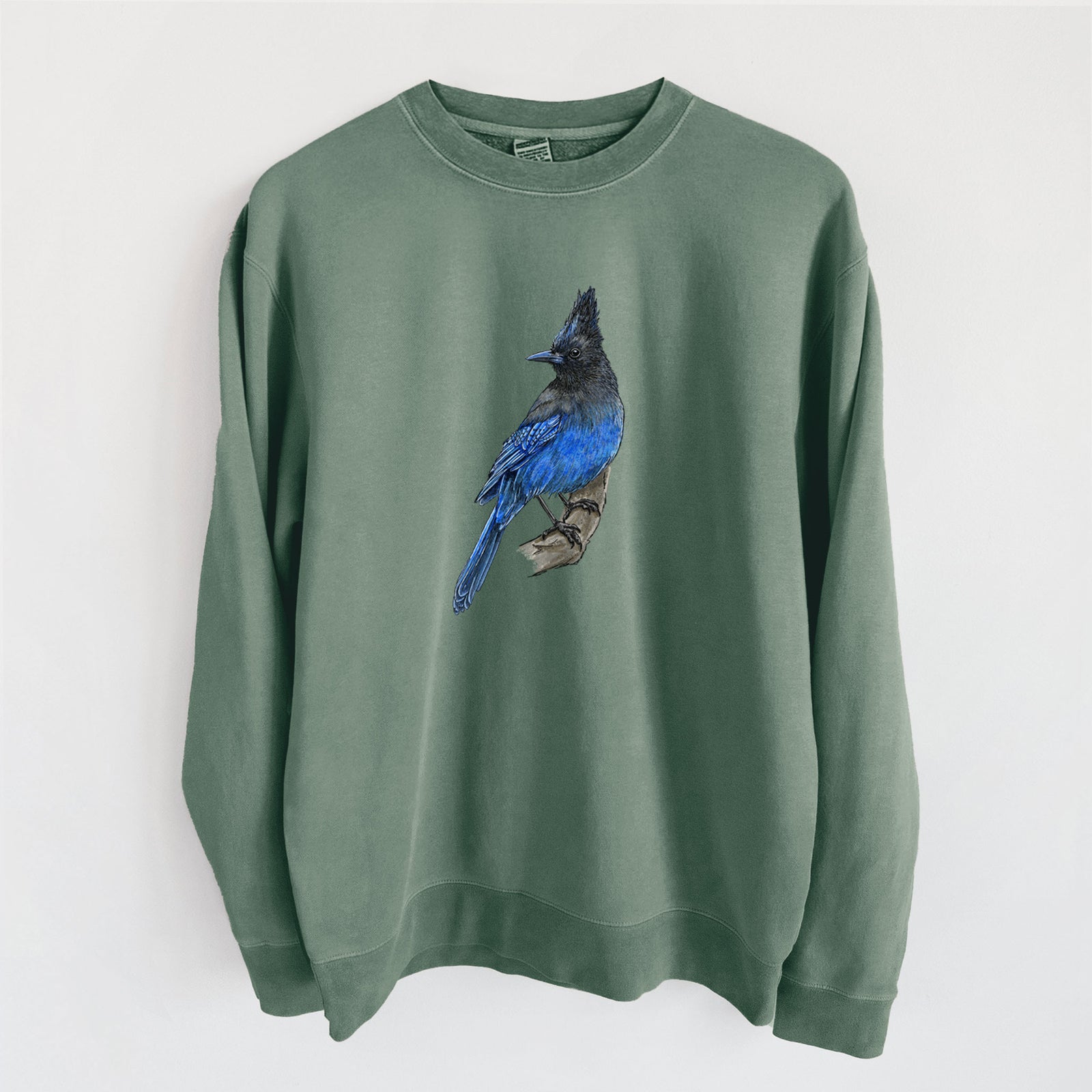 Alpine green pigment dyed crewneck sweatshirt laid flat, printed with a full-color illustration of a Steller's jay perched with its dark crest raised.