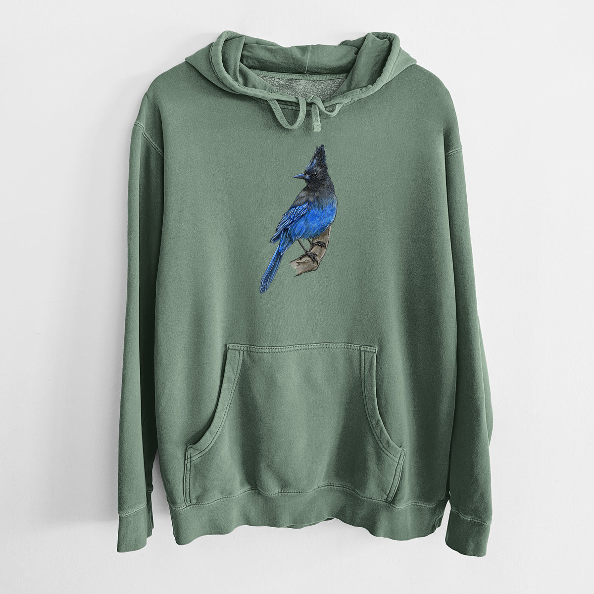 Alpine green pigment dyed hoodie laid flat, printed with a full-color illustration of a Steller's jay perched with its dark crest raised.