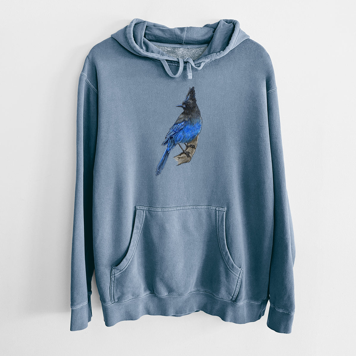 Slate blue pigment dyed hoodie laid flat, printed with a full-color illustration of a Steller's jay perched with its dark crest raised.