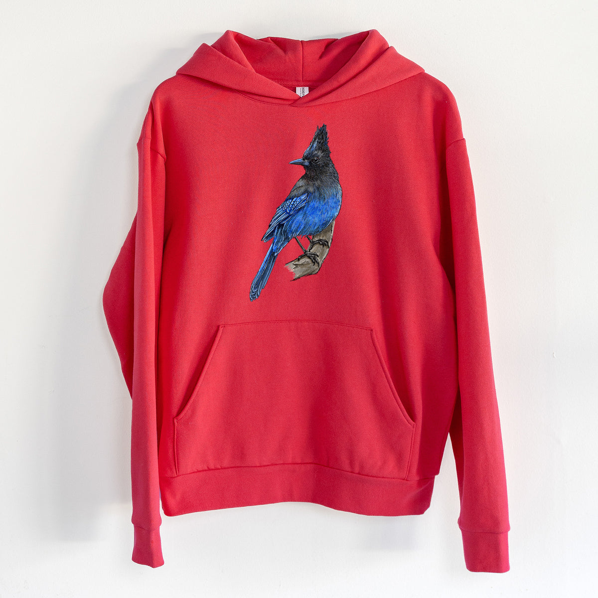 Vibrant Coastal Steller's Jay - Cyanocitta stelleri - Statement Midweight Hoodie in Cherry Red, hanging on a white wall, with a front kangaroo pocket and no drawcords.