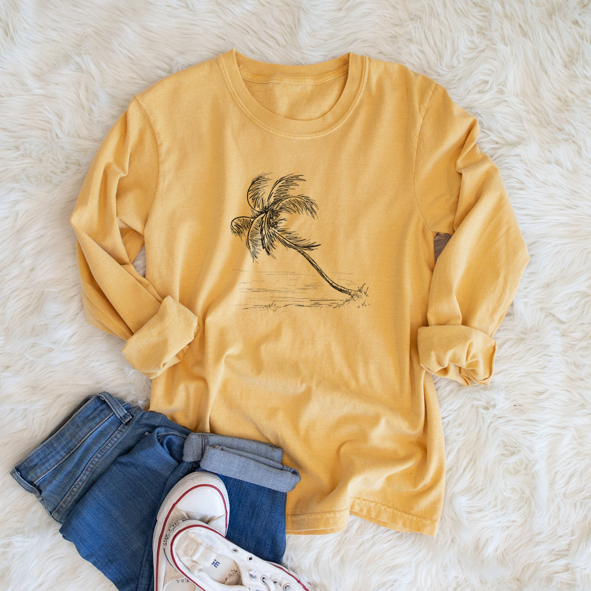 Golden wheat yellow Comfort Colors long sleeve shirt printed with a black ink illustration of a coconut palm leaning over a sandy beach, shown in a lifestyle photo.