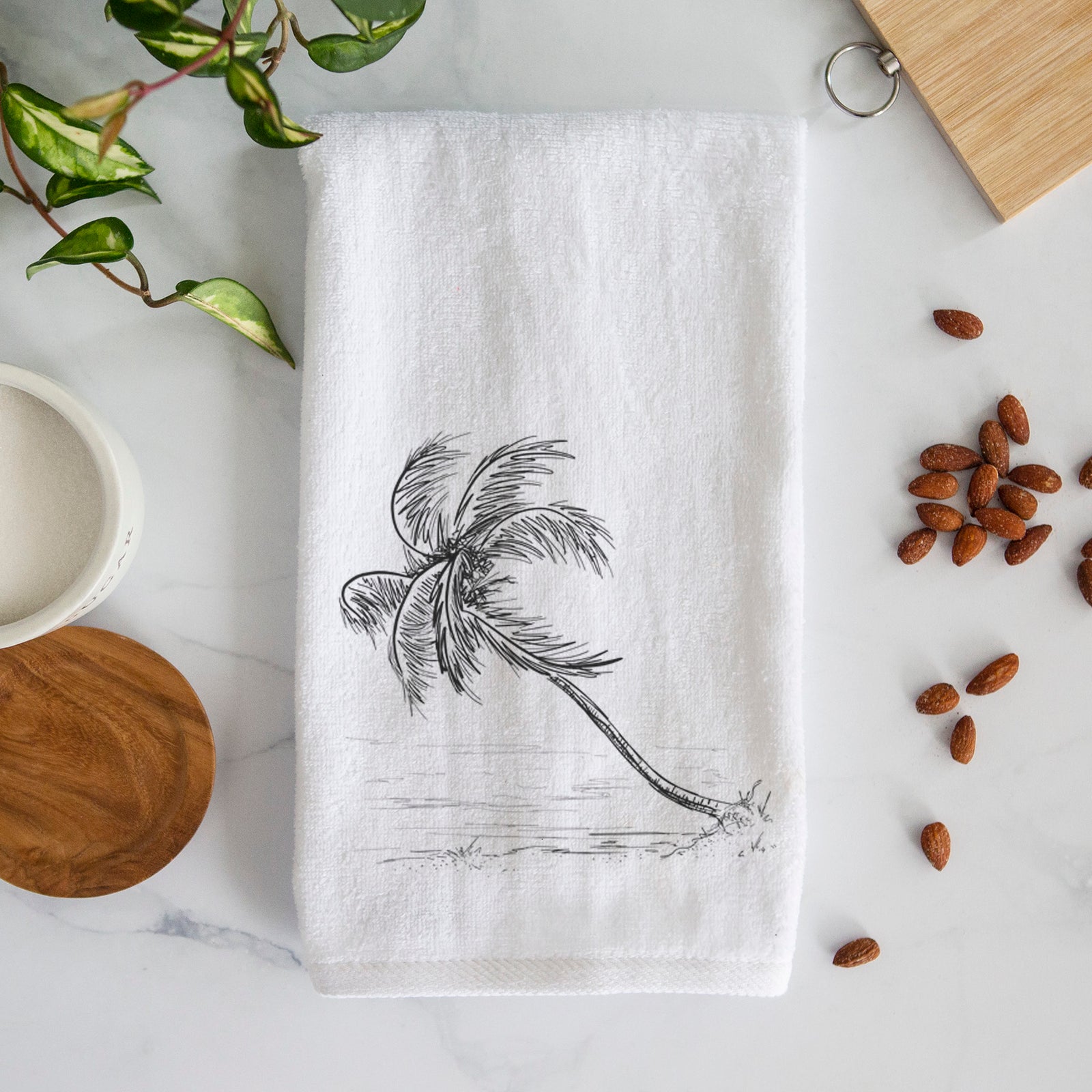 White hand towel printed with a black ink illustration of a coconut palm leaning over a sandy beach.