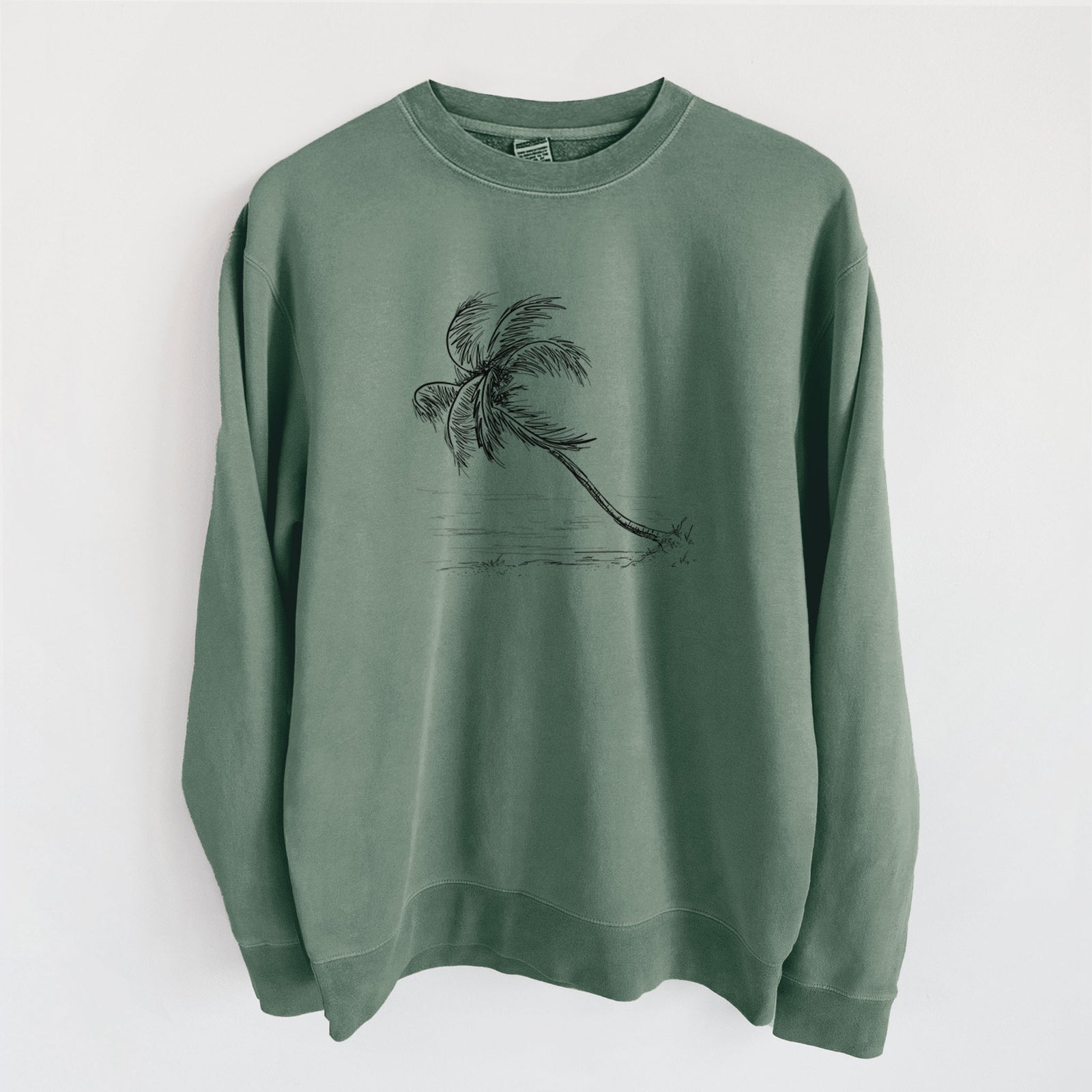 Alpine green pigment dyed crewneck sweatshirt laid flat, printed with a black ink illustration of a coconut palm leaning over a sandy beach.