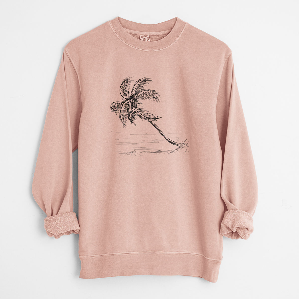 Dusty pink pigment dyed crewneck sweatshirt laid flat with the sleeves rolled, printed with a black ink illustration of a coconut palm leaning over a sandy beach.