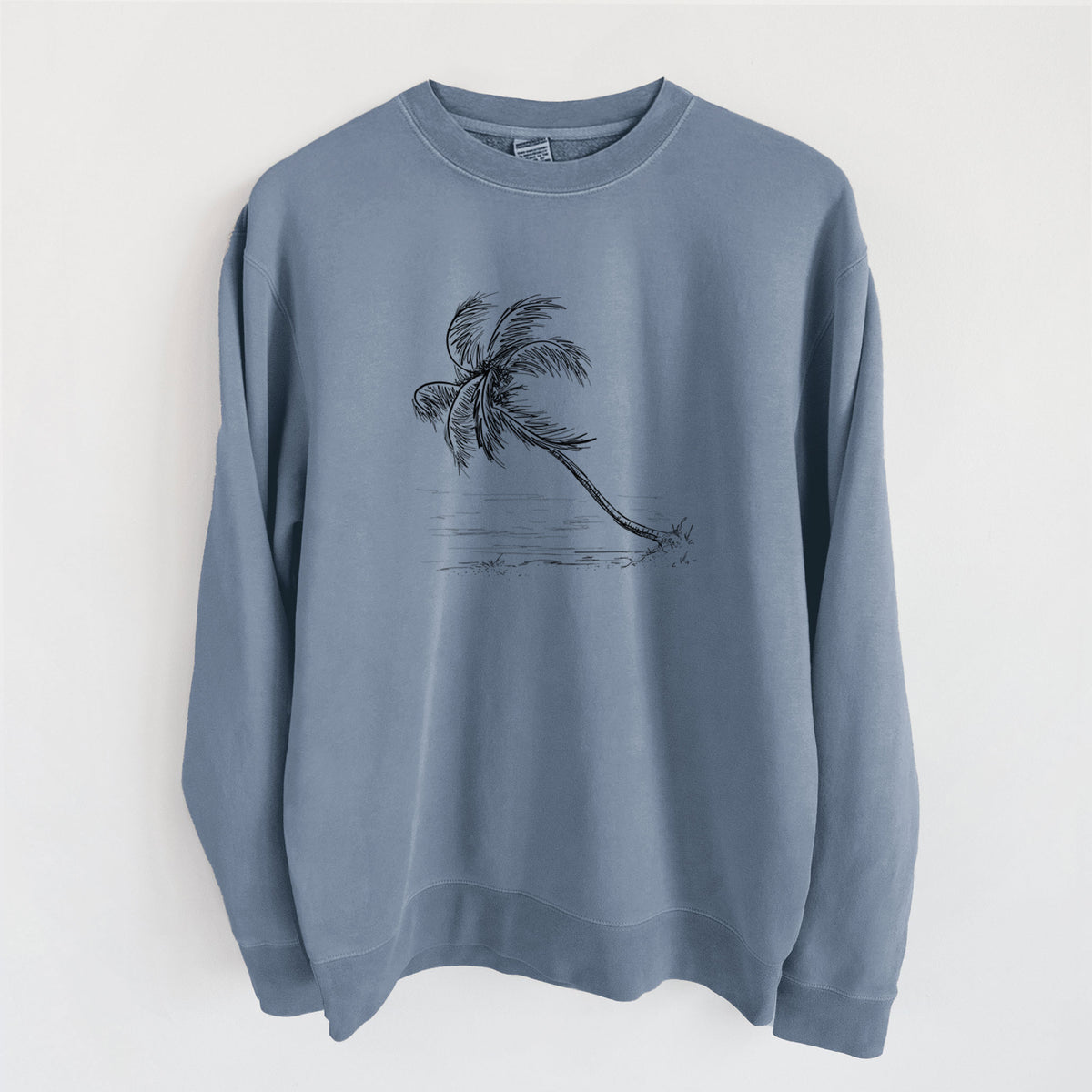 Slate blue pigment dyed crewneck sweatshirt laid flat, printed with a black ink illustration of a coconut palm leaning over a sandy beach.
