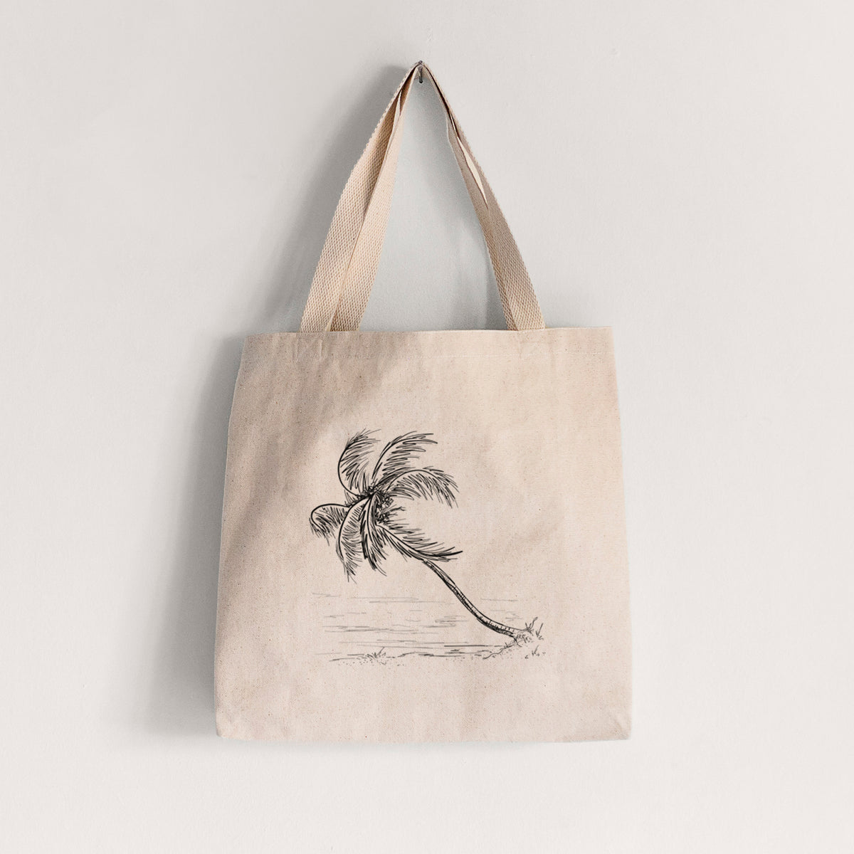 Natural canvas tote bag printed with a black ink illustration of a coconut palm leaning over a sandy beach.