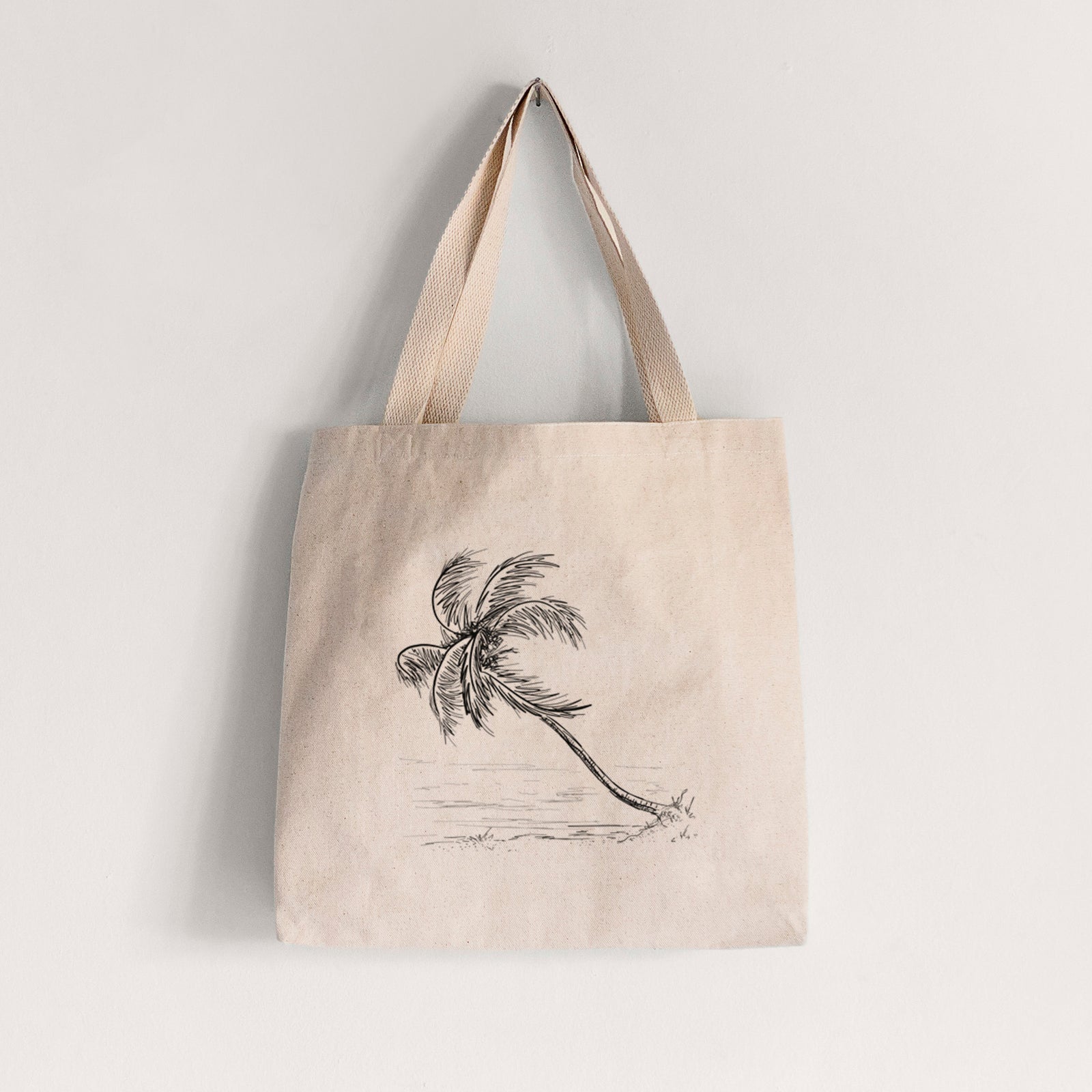 Natural canvas tote bag printed with a black ink illustration of a coconut palm leaning over a sandy beach.