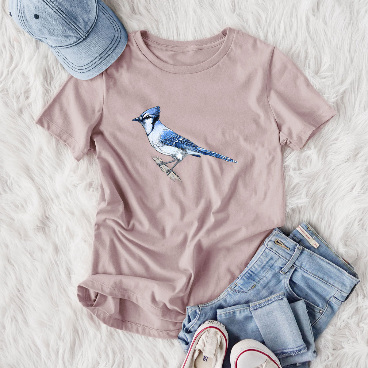 Women's relaxed fit cotton t-shirt printed with a full-color illustration of a blue jay perched on a branch, styled flat on a white faux fur rug with jeans.