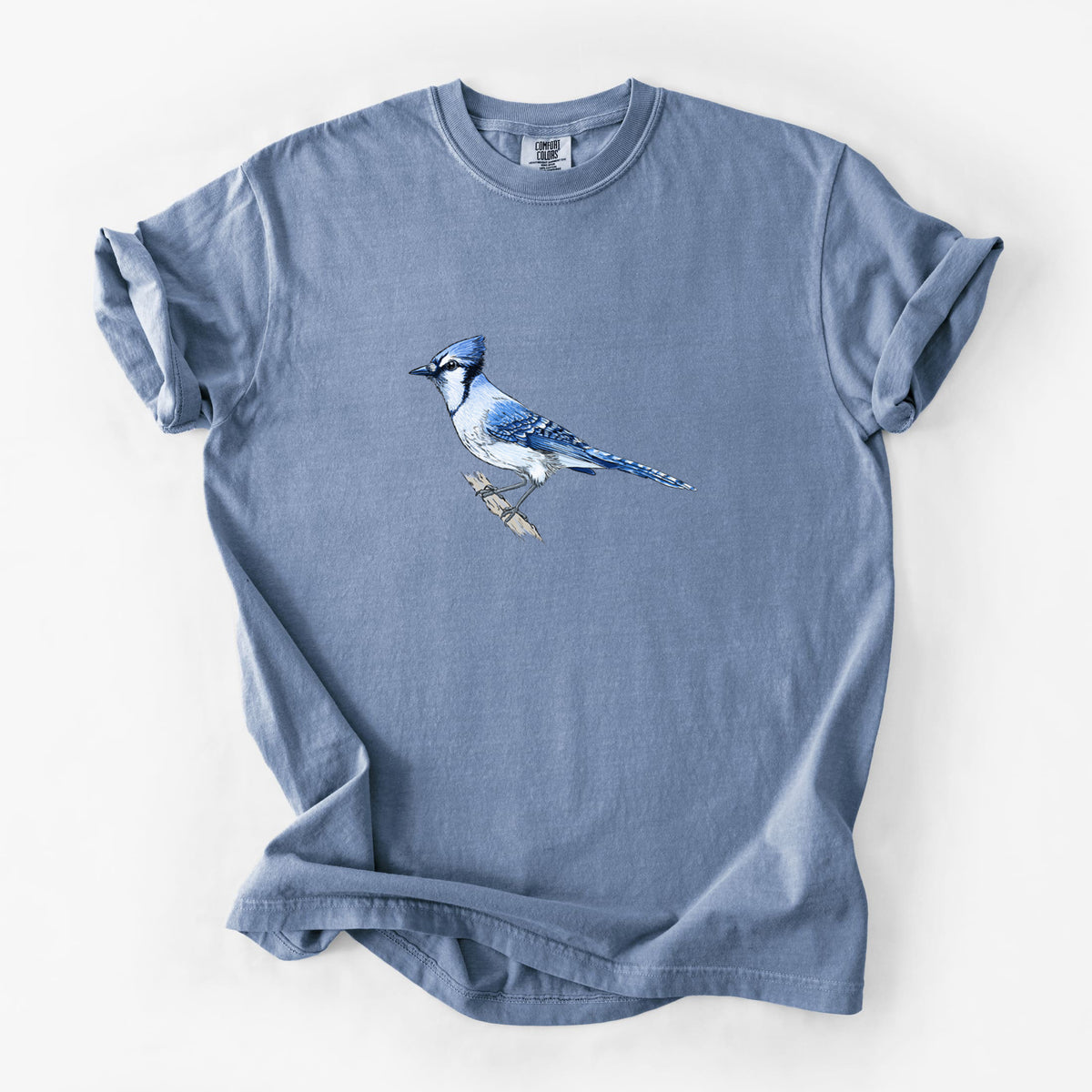 Blue jean Comfort Colors t-shirt laid flat, printed with a full-color illustration of a blue jay perched on a branch.