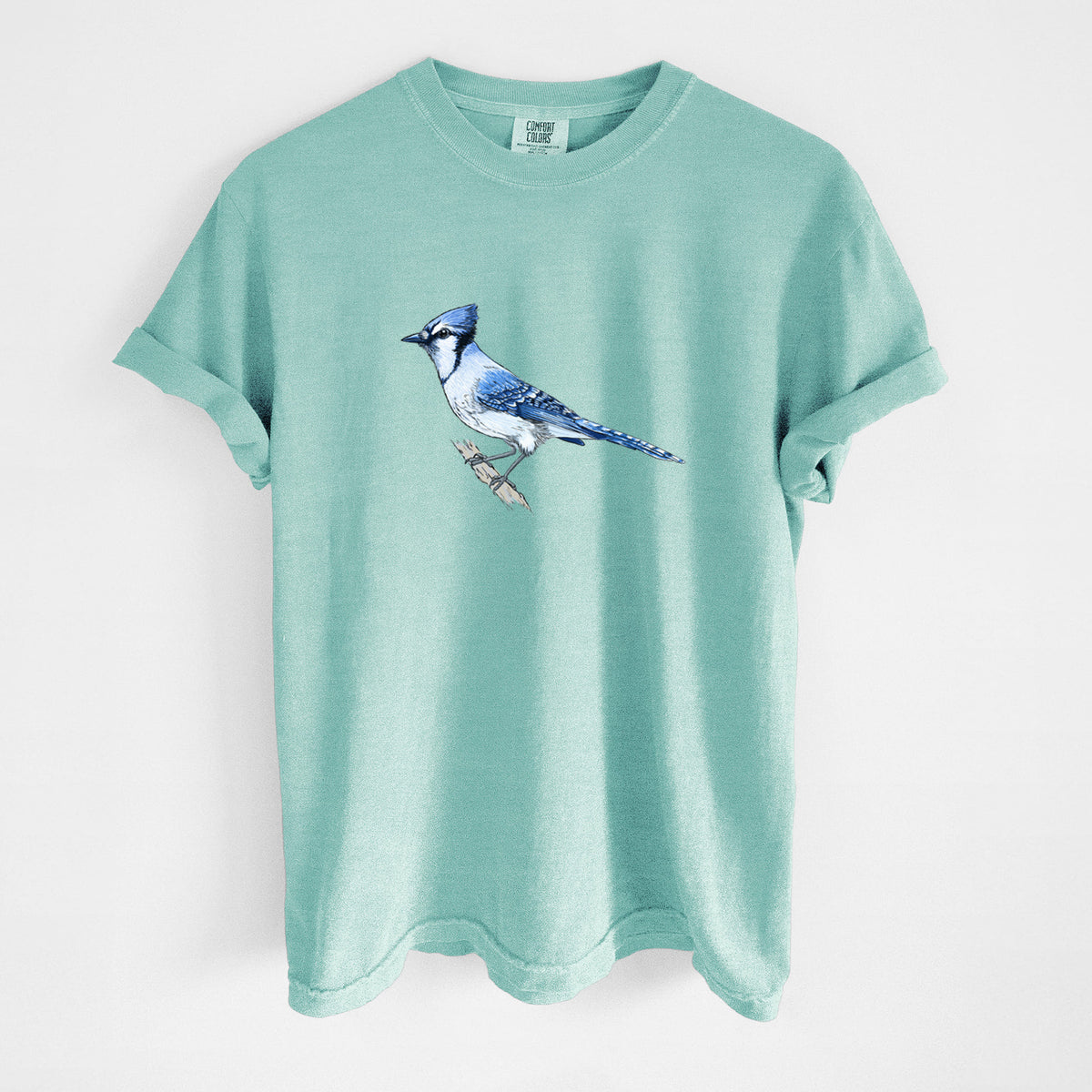 Chalky mint Comfort Colors t-shirt laid flat, printed with a full-color illustration of a blue jay perched on a branch.