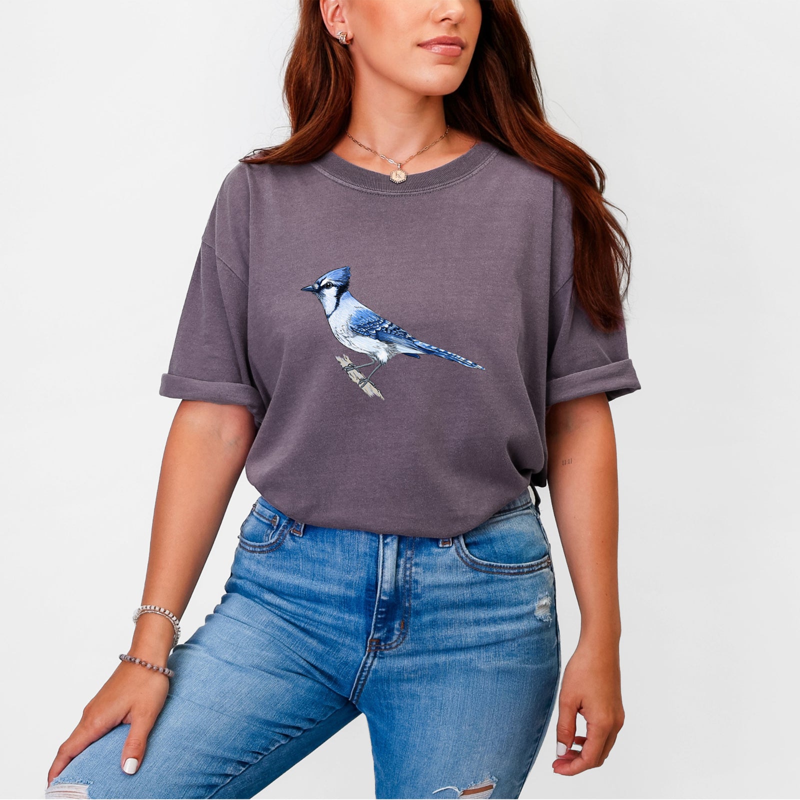 Blue jean Comfort Colors t-shirt laid flat, printed with a full-color illustration of a blue jay perched on a branch.
