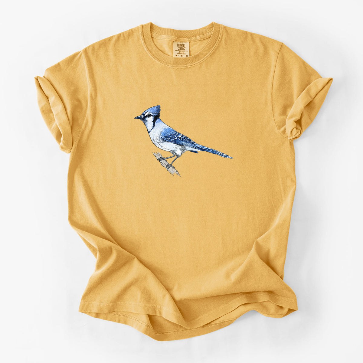 Golden wheat yellow Comfort Colors t-shirt laid flat, printed with a full-color illustration of a blue jay perched on a branch.