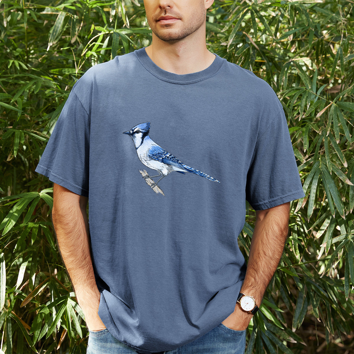 Man wearing a Comfort Colors t-shirt printed with a full-color illustration of a blue jay perched on a branch, outdoors.