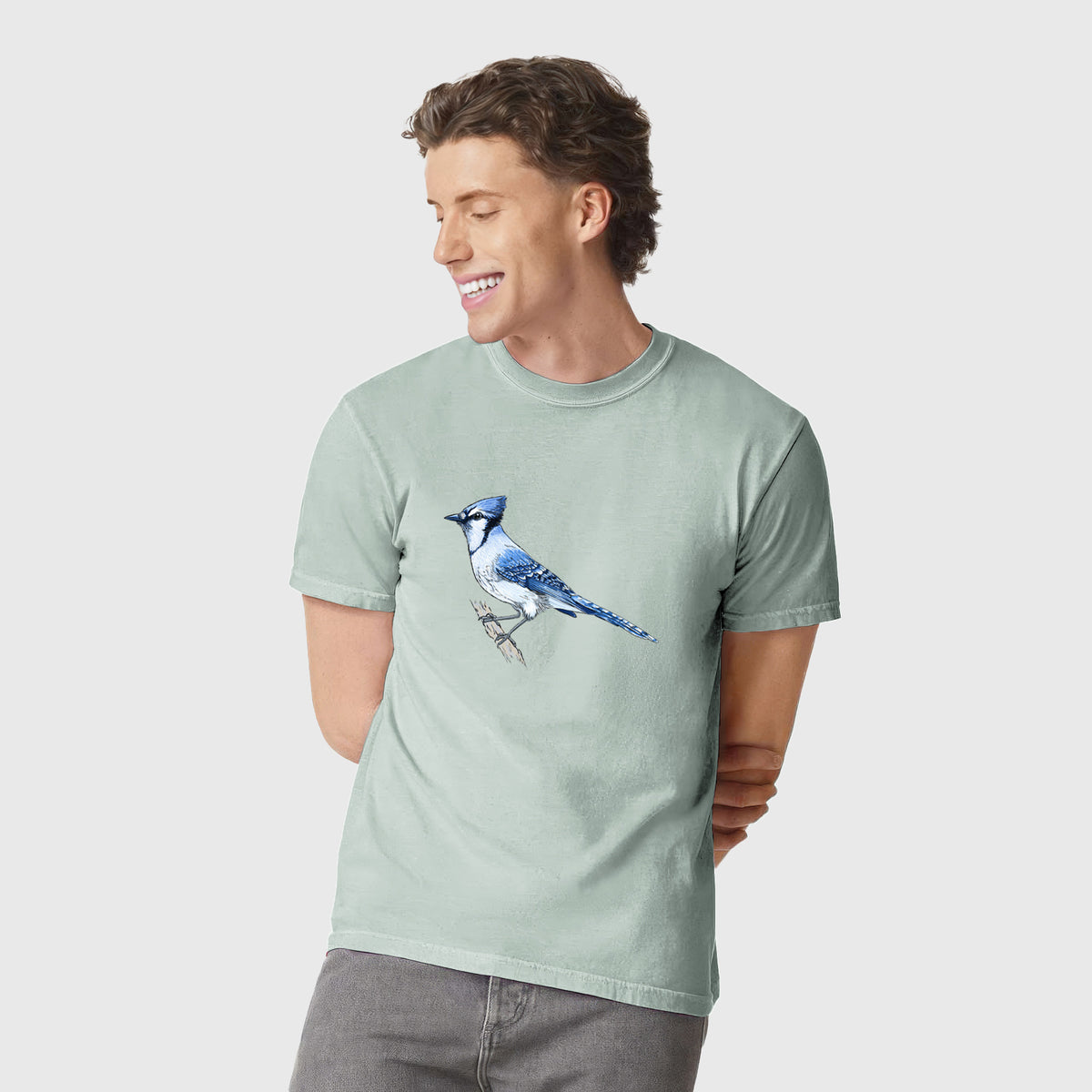 Man wearing a Comfort Colors t-shirt printed with a full-color illustration of a blue jay perched on a branch.