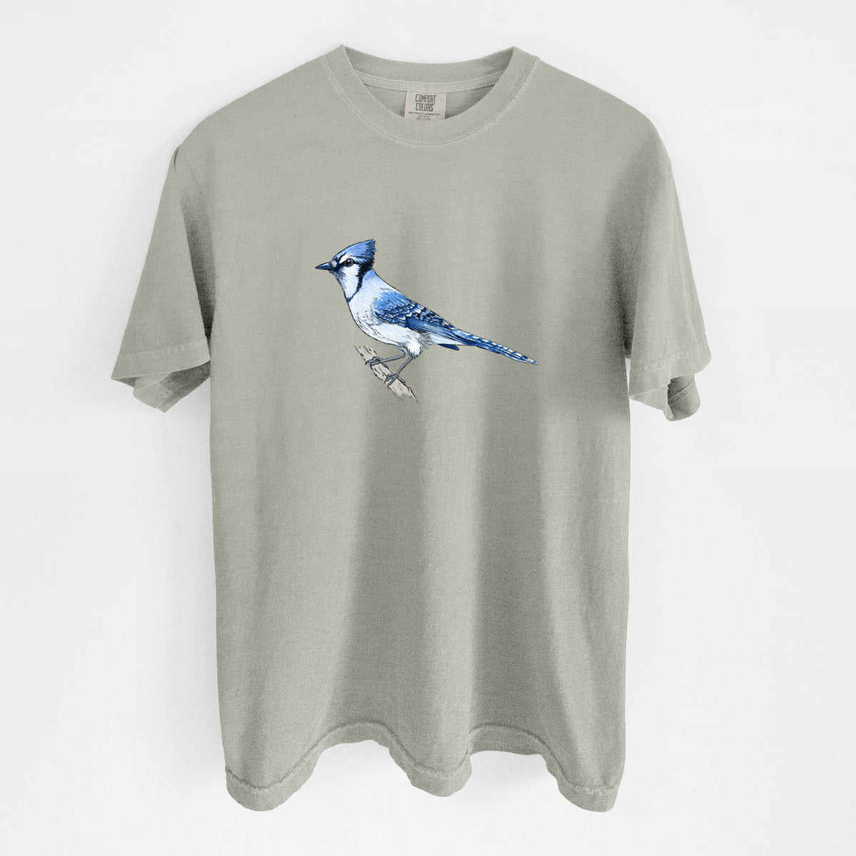 Sandstone beige Comfort Colors t-shirt laid flat, printed with a full-color illustration of a blue jay perched on a branch.