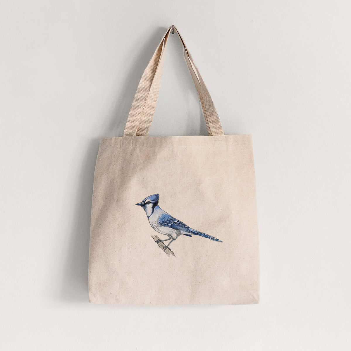 Natural canvas tote bag printed with a full-color illustration of a blue jay perched on a branch.