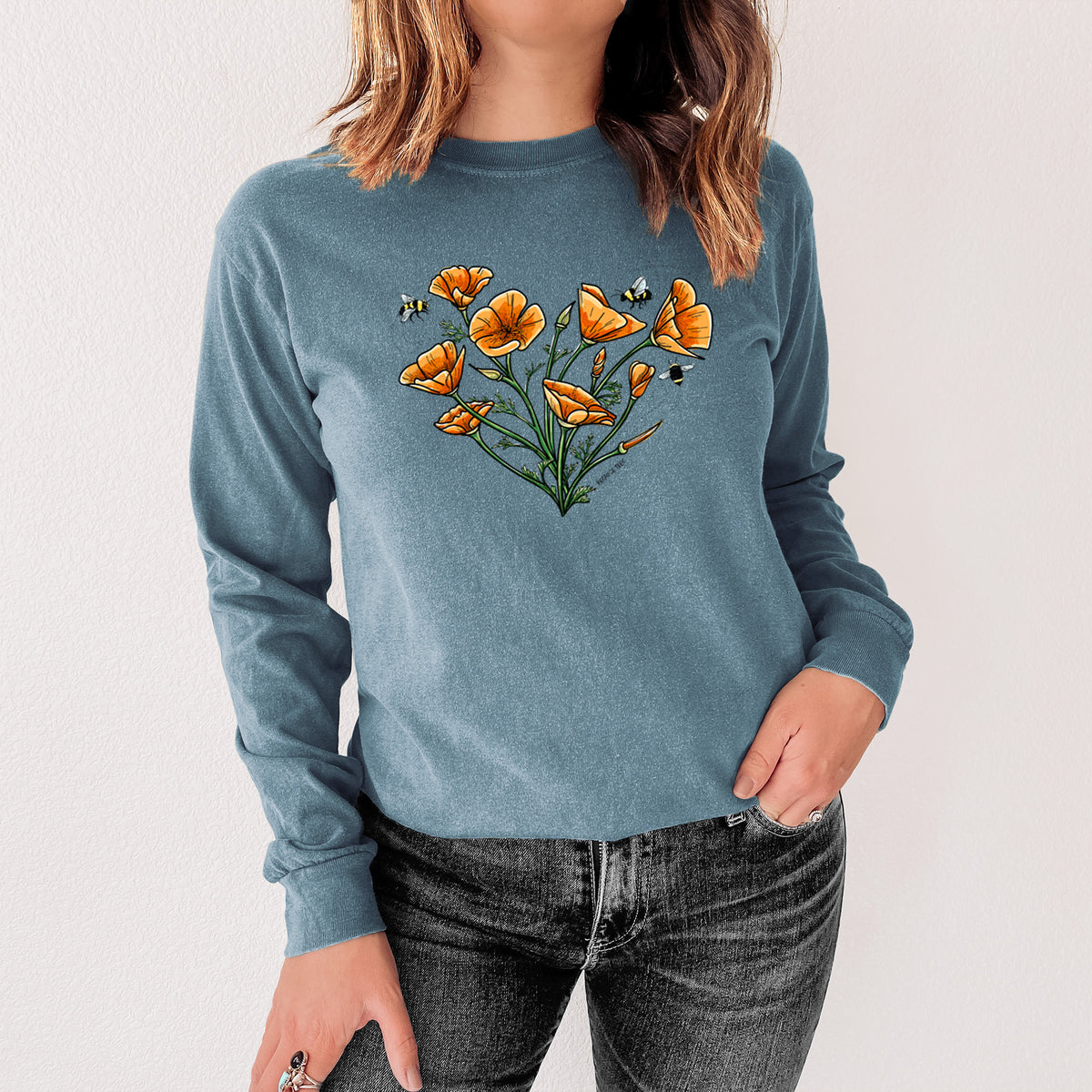 Steel blue Comfort Colors long sleeve shirt printed with a full-color bouquet of orange California poppies arranged in a heart shape, with small bees, shown in a lifestyle photo.