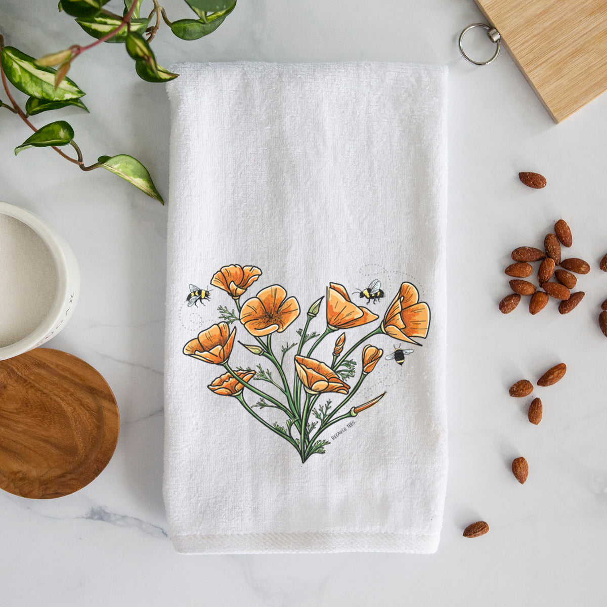 White hand towel printed with a full-color bouquet of orange California poppies arranged in a heart shape, with small bees.