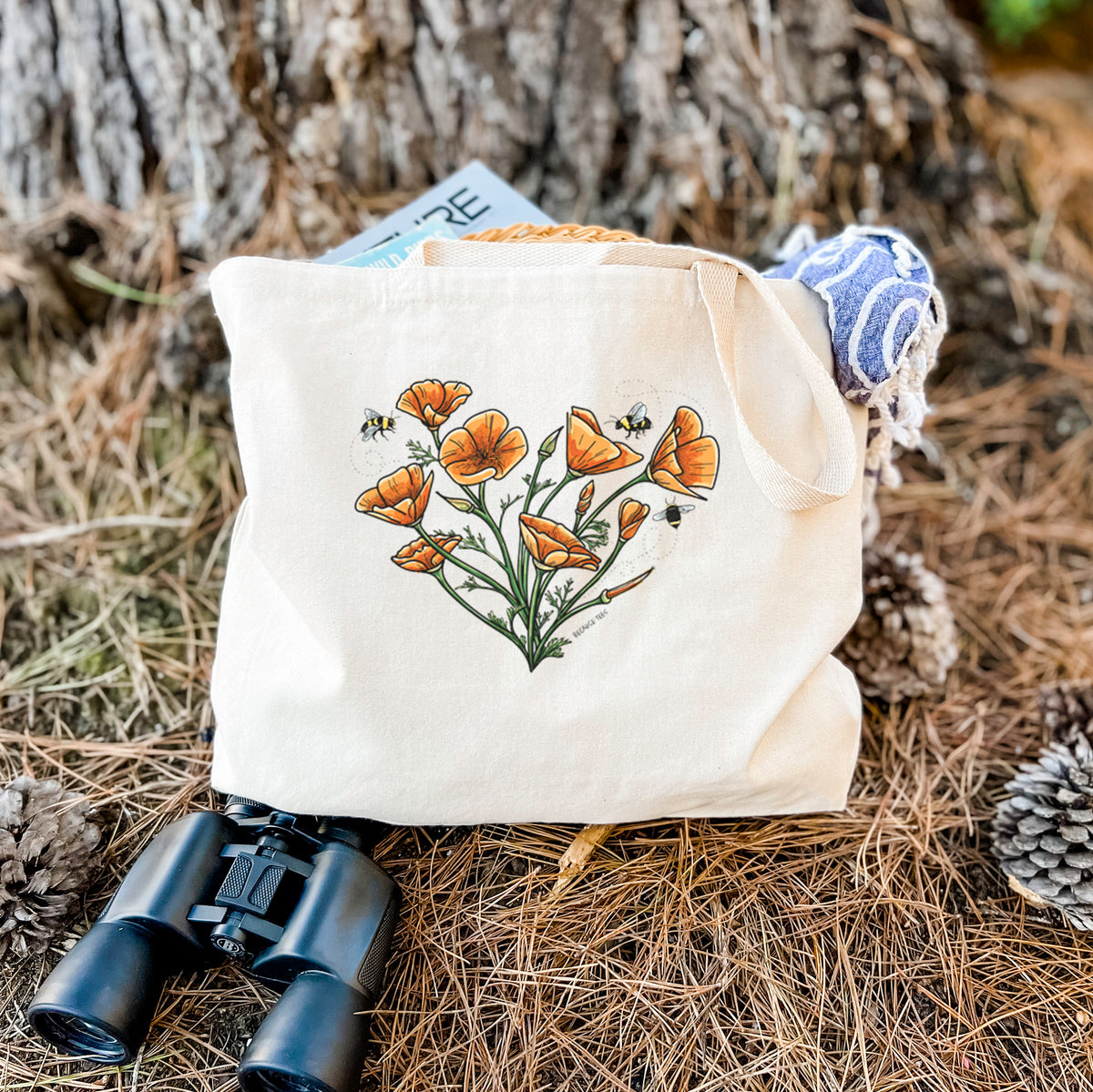 Canvas tote bag printed with a full-color bouquet of orange California poppies arranged in a heart shape, with small bees, resting on dry grass beside a pair of binoculars.