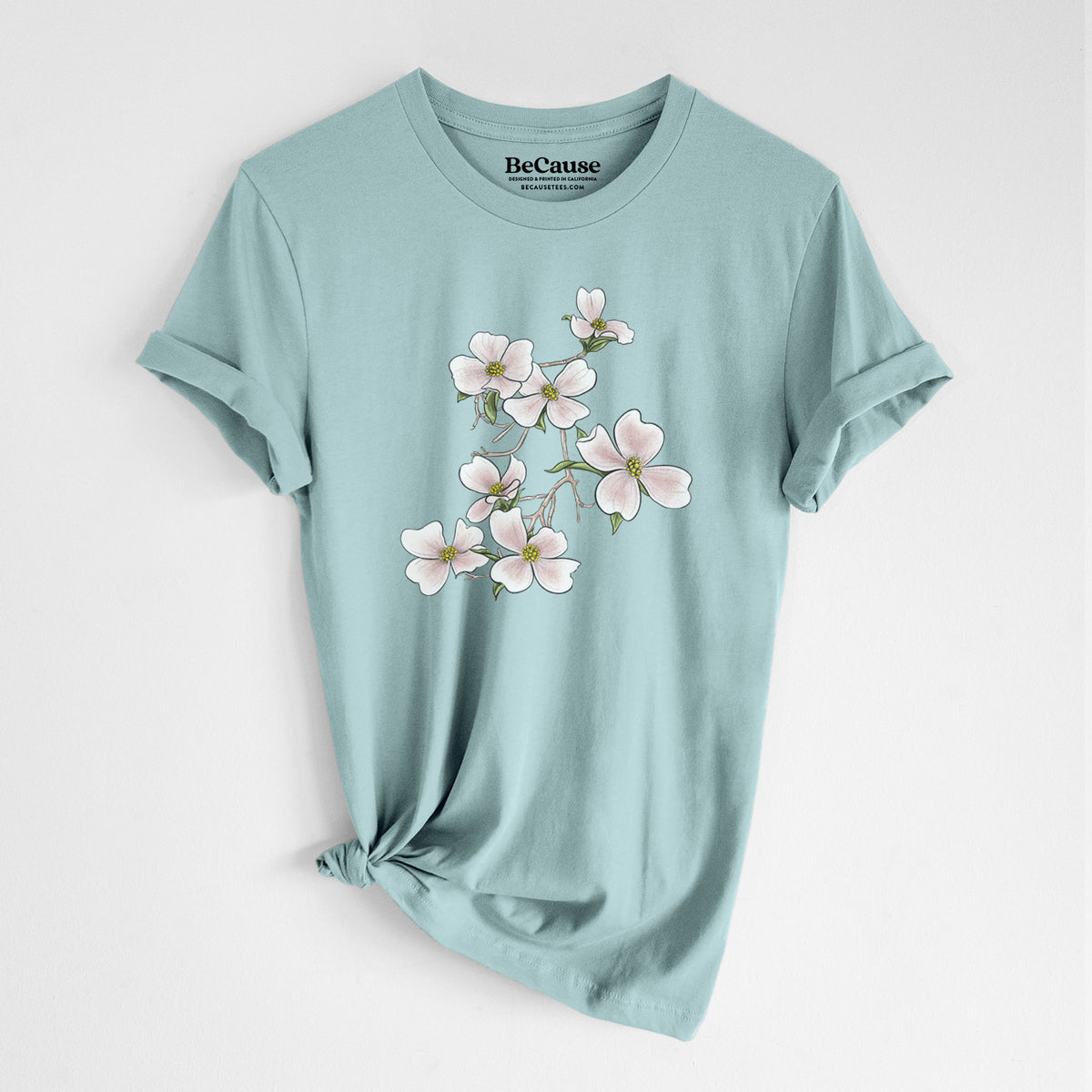 Dusty blue lightweight cotton t-shirt laid flat with the sleeves rolled, printed with a full-color illustration of pink and white dogwood blossoms on a branch.