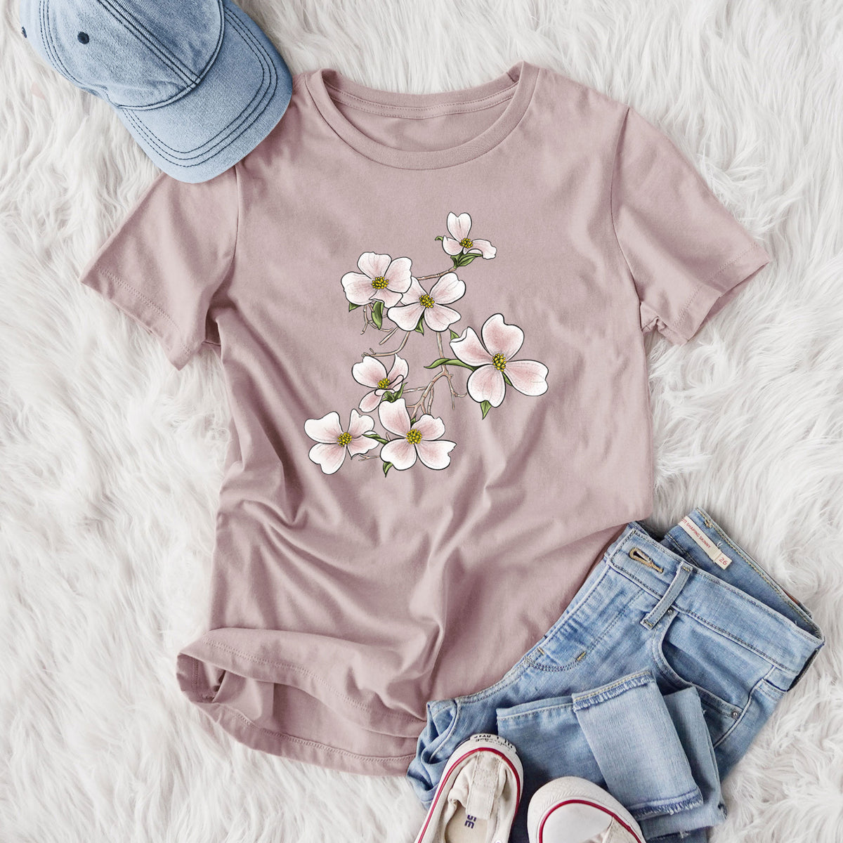 Women's relaxed fit cotton t-shirt printed with a full-color illustration of pink and white dogwood blossoms on a branch, styled flat on a white faux fur rug with jeans.