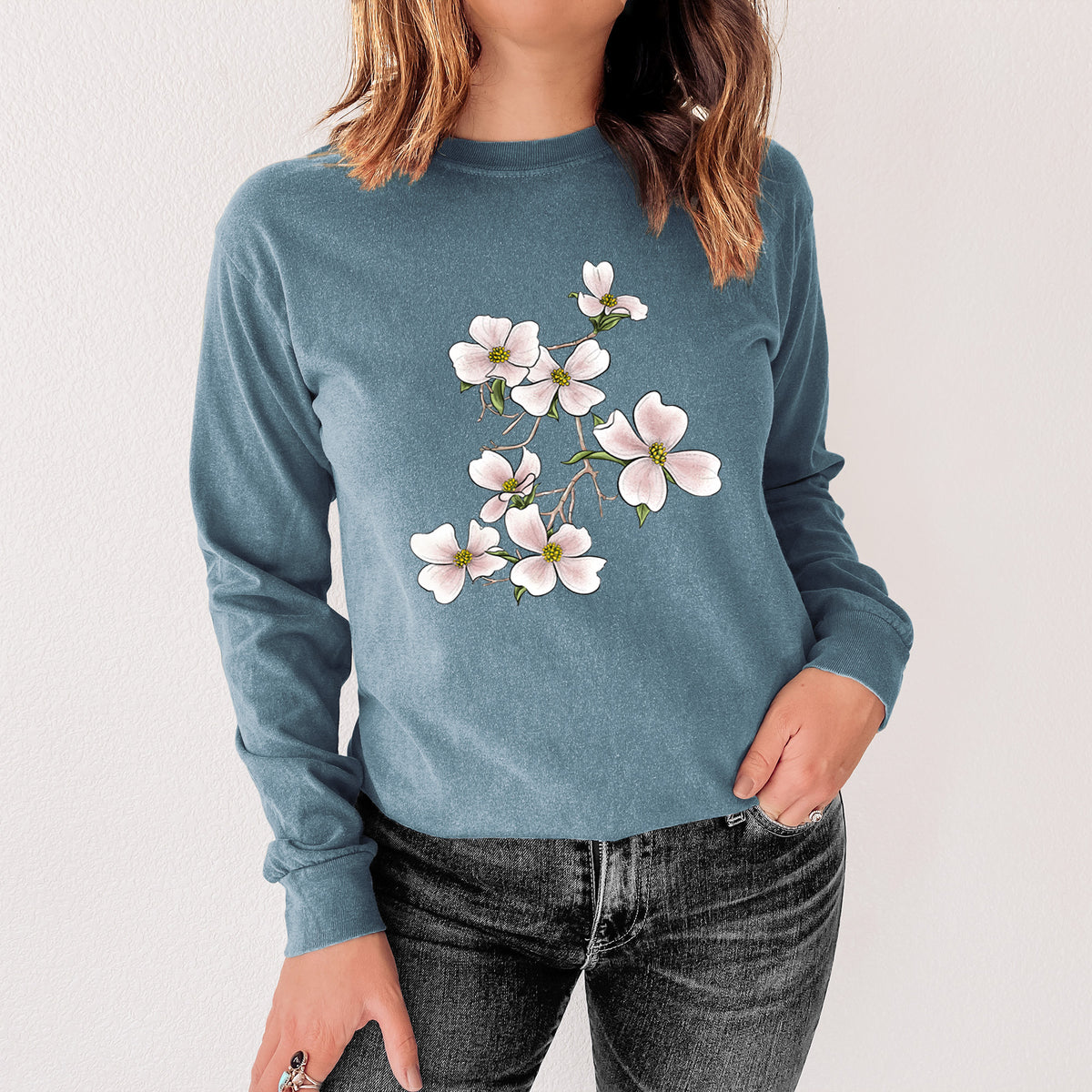Steel blue Comfort Colors long sleeve shirt printed with a full-color illustration of pink and white dogwood blossoms on a branch, shown in a lifestyle photo.