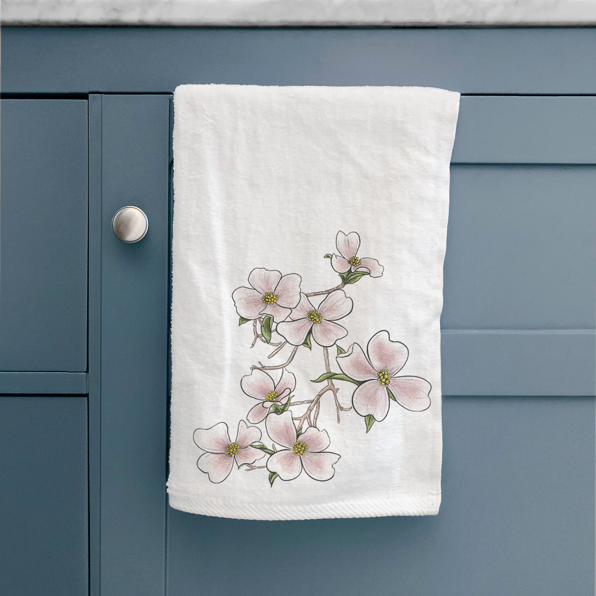White hand towel printed with a full-color illustration of pink and white dogwood blossoms on a branch, hanging on a cabinet door.