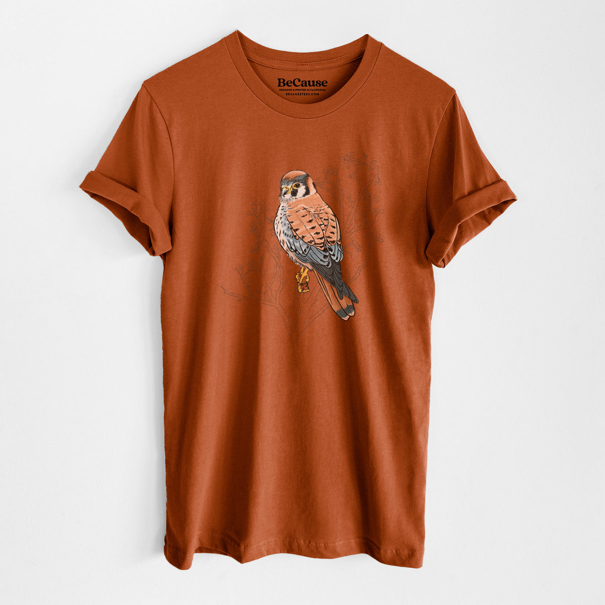 Autumn lightweight cotton t-shirt laid flat, printed with a full-color illustration of an American kestrel perched among pale branches.