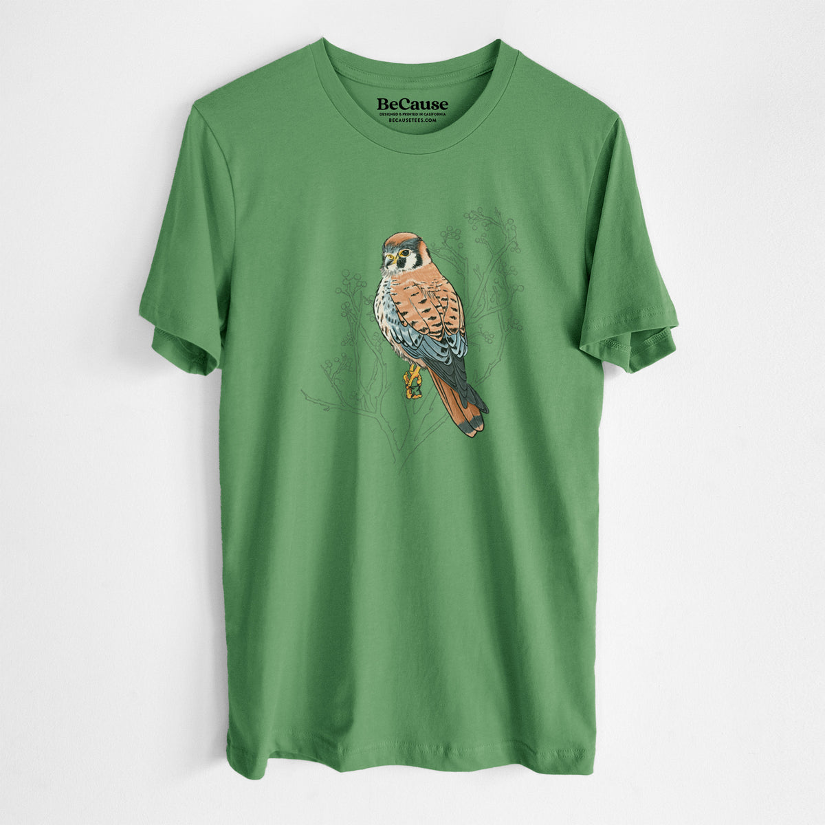 Leaf green lightweight cotton t-shirt laid flat, printed with a full-color illustration of an American kestrel perched among pale branches.