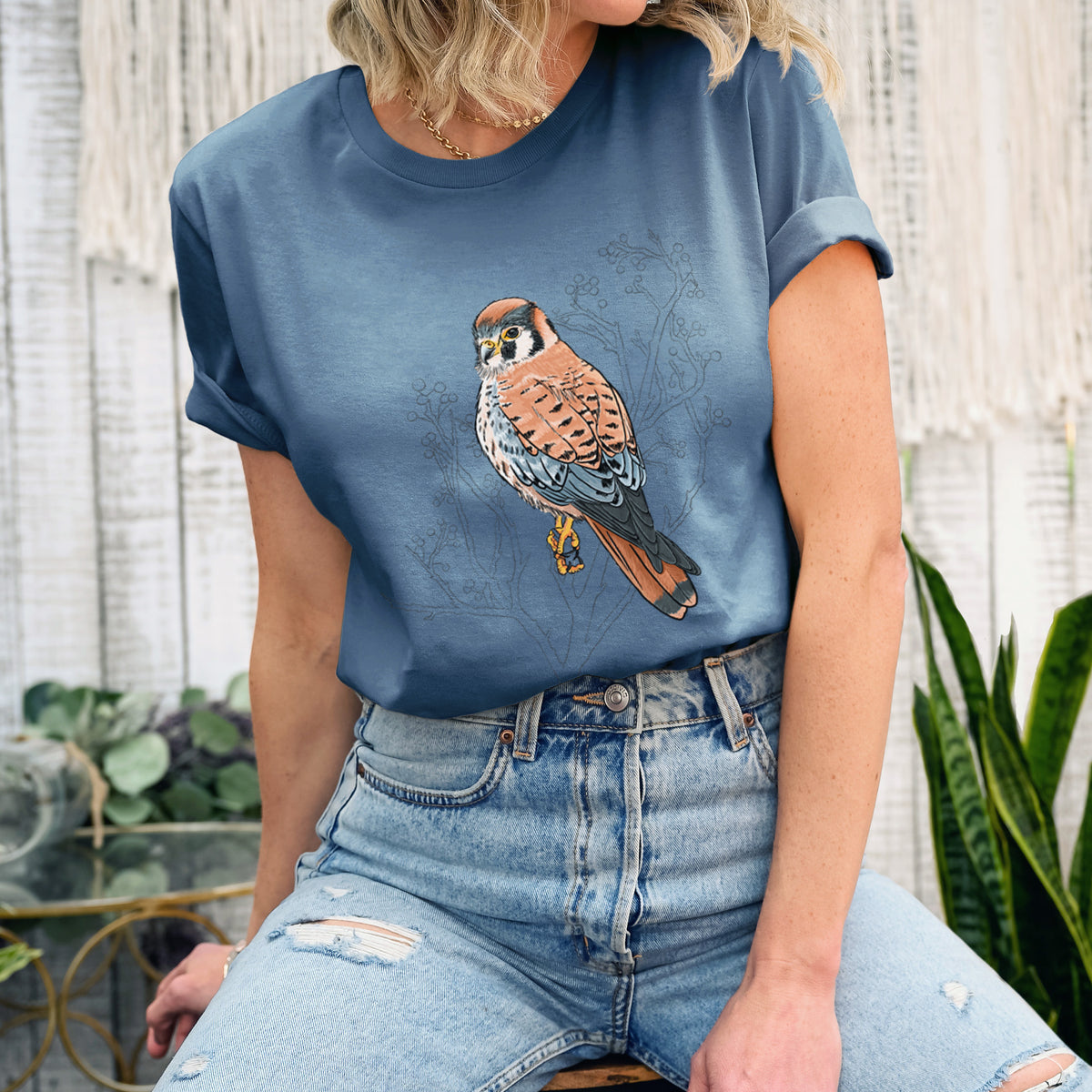 Woman wearing a steel blue lightweight cotton t-shirt printed with a full-color illustration of an American kestrel perched among pale branches.