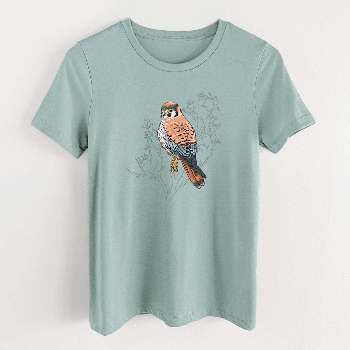 Dusty blue women's relaxed fit cotton t-shirt laid flat, printed with a full-color illustration of an American kestrel perched among pale branches.